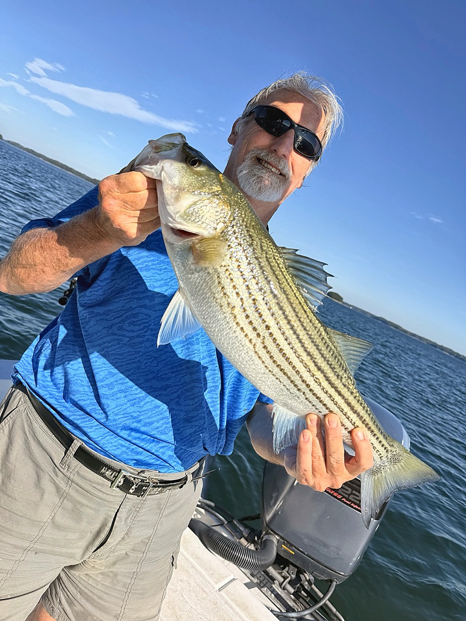 Lake Lanier Striper Fishing Report – October 12, 2026 Longtime client holding a Lake Lanier striped bass under bluebird skies